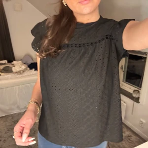 Svart blus med spetsdetaljer - Säljer en stilren svart blus med spetsdetaljer. Blusen har korta ärmar och en lös passform, perfekt för en avslappnad men elegant look.