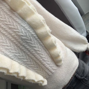 Vit stickad tröja från Bubbleroom - Säljer en superfin vit stickad tröja från Bubbleroom med volangdetaljer längs framsidan. Tröjan har ett snyggt stickat mönster och långa ärmar. Perfekt för kyliga dagar! 💫