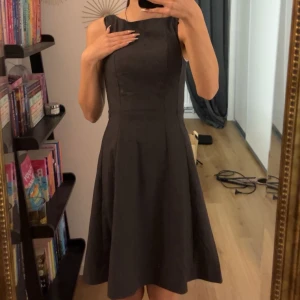 Grå klänning - Grå svart klänning med en elegant och kostymig vibe. Klänningen har en figurnära passform upptill och en utsvängd kjol som ger en fin silhuett. Perfekt för olika tillfällen och lätt att matcha med accessoarer.
