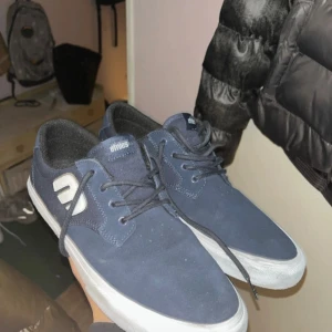 Skate skor från Etnies - Skate skor från Etnies med vit sula och snörning. Perfekta för en avslappnad stil. Skorna har en diskret logga på sidan och är tillverkade i mocka. Har skejtat dem 5 gånger 