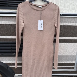 Beige ribbad klänning från NA-KD - Säljer en stilren beige ribbad klänning från NA-KD. Klänningen har en enkel design med långa ärmar och en rund halsringning. Perfekt för en minimalistisk look. Passar bra till både vardag och speciella tillfällen.