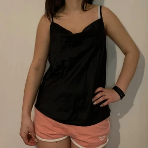 Svart satinlinne - Snyggt svart linne i satin med smala axelband. Perfekt för en stilren look.