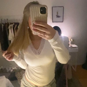 Vit långärmad topp med spetsdetalj - Säljer en stilren vit långärmad topp med vacker spetsdetalj vid halsringningen. Perfekt för en elegant och bekväm look.