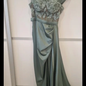 Olivgrön långklänning med spetsdetaljer - Elegant Olivgrön långklänning med vackra spetsdetaljer på överdelen. Klänningen har en draperad kjol och en axelbandslös design som ger en sofistikerad look. Perfekt för speciella tillfällen. Vi kan diskutera priset 