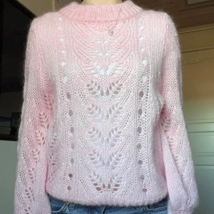 Rosa stickad tröja - Säljer en söt rosa stickad tröja i mohair med ett vackert hålmönster. Tröjan har långa ärmar och en rund halsringning, perfekt för kyligare dagar. Den är både mysig och stilren, vilket gör den till ett måste i garderoben. Passar perfekt till jeans eller kjol för en avslappnad look.