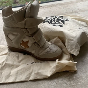 Beige sneakers från Isabel Marant - Snygga beige sneakers från Isabel Marant med en stjärndetalj i brunt. Skorna har en hög design med kardborreband och en gummisula. Perfekta för en trendig look. I ny skick och orginal påse ingår! nypris 6000kr🌟💋