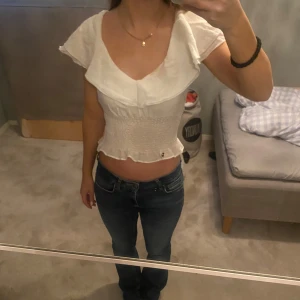 Vit topp - Säljer en söt vit topp/blus med volangdetaljer och smockad midja. Toppen har en öppen rygg med knytband och korta ärmar. Sååå fin och perfekt till sommaren😊💕pris går att diskutera men använd gärna annars köp nu😊