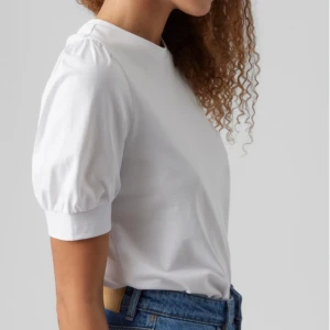 Vit kortärmad topp - Säljer en stilren vit topp med korta puffärmar. Toppen har en rund hals och är tillverkad i ett mjukt bomullsmaterial. Perfekt för en avslappnad look. Från VERO MODAs egna märke AWARE