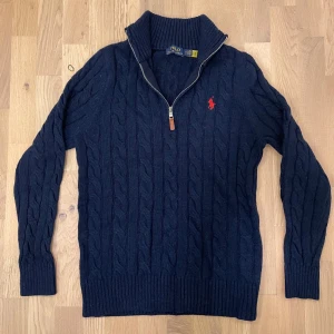 Ralph lauren half zip - Säljer en stilren mörkblå stickad tröja från Polo Ralph Lauren med kabelstickat mönster och dragkedja vid halsen. Tröjan har långa ärmar och en broderad logotyp på bröstet. Perfekt för kyliga dagar! Passar dig med storlek S! Priset är diskuterbart