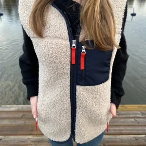 Beige dunväst - Beige teddyväst med marinblåå fickor och orange/röda dragkedjor