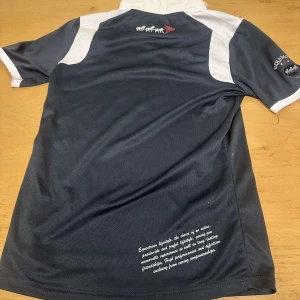 Svart och vit rid t-shirt med text - Snygg svart t-shirt med vita detaljer och text på ryggen. Perfekt för dig som ska tävla. Kortärmad design med en sportig look.