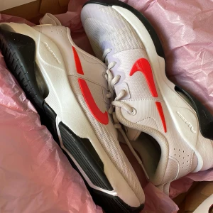 Vita Nike sneakers med röd detalj - Snygga vita Nike sneakers med en iögonfallande röd swoosh på sidan. Skorna har en bekväm passform med snörning och en svart sula som ger bra grepp. Perfekta för en sportig look. Skriv om ni är intresserade <3