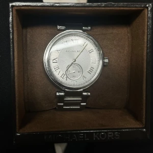 Silverfärgad klocka från Michael Kors - Elegant silverfärgad klocka från Michael Kors med romerska siffror och en stilren urtavla. Pris går att diskuteras vid snabb affär 🩶