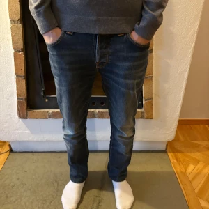 Blå jeans från Nudie Jeans - Snygga blå jeans från Nudie Jeans med klassisk femficksdesign och orange sömmar. De har en normal passform och är perfekta för en avslappnad stil. Jeansen har en dragkedja och knapp i gylfen.
