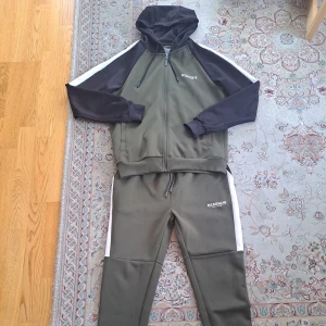 McKenzie tracksuit - Säljer ett snyggt träningsset från McKenzie i olivgrönt och svart med vita detaljer. Setet består av en hoodie med dragkedja och matchande byxor. Perfekt för träning eller en avslappnad dag. De är använda men är ändå i relativt bra skick.