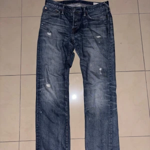 Blå Evisu Jeans med slitningar - Säljer ett par klassiska blå jeans från Evisu med slitningar för en cool look. Byxorna har en straight passform och har egengjorda slitningar från tidigare ägare. Fåtal gånger använda.