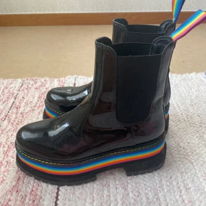 Kurt geiger boots - Snygga svarta glansiga boots med regnbågsfärgad sula och dragflikar från kurt geiger. Perfekta för att sätta färg på din outfit. De har en robust sula med bra grepp och elastiska sidopaneler för enkel påtagning. Använda max 2 gånger, har en liten skrapa som knappt syns! 🎀 