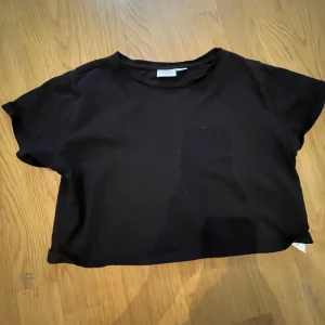 Svart croppad t-shirt från Gina Tricot - Säljer en svart croppad t-shirt från Gina Tricot. Den har en enkel design med korta ärmar och rund halsringning. Perfekt för en avslappnad stil. (Den är väldigt kort, måste ha linne under om man vill såklart)