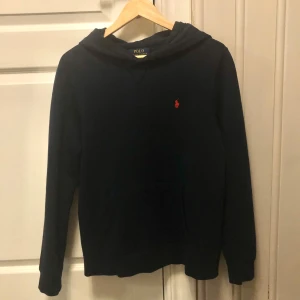Mörkblå hoodie från Ralph Lauren - Säljer en stilren mörkblå hoodie från Ralph Lauren med det klassiska röda logotypbroderiet på bröstet. Tröjan har en bekväm passform med långa ärmar och en praktisk huva. Perfekt för en avslappnad look. Tröjan är i barn XL men passar perfekt för Xs/S. Fråga om du har några funderingar! ☺️
