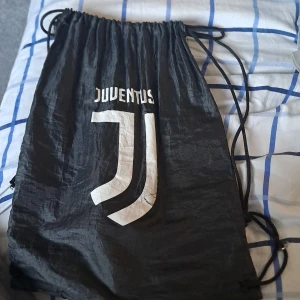 Svart gympapåse med Juventus-logga - Säljer en svart gympapåse med Juventus-logga i vitt. Perfekt för att bära med sig träningskläder eller andra småsaker. Påsen har snörning för enkel stängning och bärande.