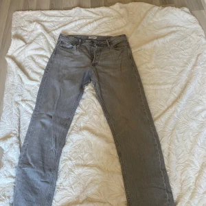 Grå jeansbyxor från Jack and Jones - Snygga grå jeansbyxor från Jack and Jones med klassisk design. De har en rak passform och knappar i gylfen. Perfekta för en stilren look.