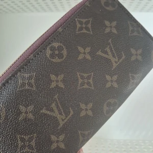 Brun plånbok med monogram - Snygg brun plånbok med klassiskt monogrammönster. Den har en dragkedja upptill och är perfekt för att hålla dina kort och kontanter organiserade. En stilren accessoar för alla tillfällen.
