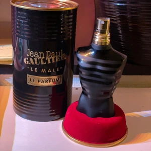 Jean Paul Gaultier Le Male Le Parfum 75ml - Elegant parfymflaska formad som en manlig torso i svart med grå ränder. Kommer i en stilren svart metallburk med guldtext. Flaskan rymmer 75 ml och har en lyxig känsla. Perfekt för den som vill ha en sofistikerad doftupplevelse. Ca25 ml kvar