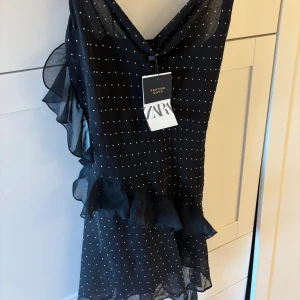 Svart prickig klänning från Zara - Snygg svart klänning från Zara med små vita prickar och volangdetaljer. Helt oanvänd 