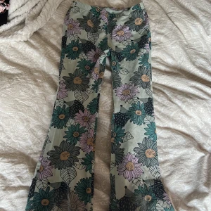 Blommiga byxor från Ellos - Snygga blommiga byxor från Ellos i storlek 122/128. Byxorna har ett färgglatt mönster med stora blommor i lila, grönt och beige. Perfekta för att liva upp garderoben med en färgklick! På sista bilden kan man se en liten fläck som är vid igelkotten ungefär! Vet ej om de går bort i tvätt därav priset