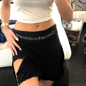 Svart kjol från Dolce & Gabbana - Snygg svart kjol från Dolce & Gabbana med glittrande detaljer i midjan. Kjolen har en slits på sidan som ger en extra touch. Perfekt för att skapa en stilren look.