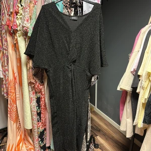 Svart glittrig klänning från Define - Snygg svart glittrig klänning från Define med v-ringning. Klänningen har korta ärmar och en elegant, figursydd passform som passar perfekt för festliga tillfällen.