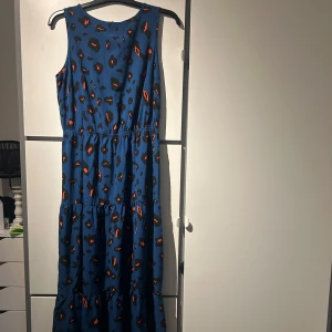 Blå ärmlös klänning med leopardmönster - Snygg blå långklänning med ett coolt leopardmönster i svart och orange. Klänningen är ärmlös och har en avslappnad passform med resår i midjan för en bekväm look. Perfekt för en trendig stil! Knappt använd