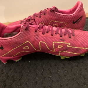 Rosa Nike AIR ZOM fotbollskor - Säljer ett par rosa Nike fotbollsskor med snörning och en iögonfallande design. Skorna har gula detaljer och en slitstark sula som ger bra grepp på planen. Populära bland stora fotbollsstjärnor som bland annat Ronaldo.