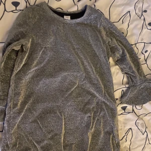 Glittrig klänning  - Säljer en glittrig klänning med långa ärmar. Perfekt för att lysa upp vilken outfit som helst. Klänning har en rund halsringning och är i ett mjukt material som känns skönt mot huden. Passar bra till både vardag och festliga tillfällen.