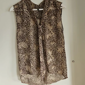 Leopardmönstrad ärmlös blus - Snygg ärmlös blus med leopardmönster och knytband framtill. Perfekt för en trendig look. Liten i storlek. 