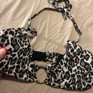 Leopardmönstrad bikiniöverdel med ringdetalj - Trendig bikiniöverdel med leopardmönster och snygg ringdetalj framtill. Den har knytband runt nacken och en justerbar spänne i ryggen för perfekt passform. Perfekt för en dag på stranden eller vid poolen. Från Gina tricot🤍🤎