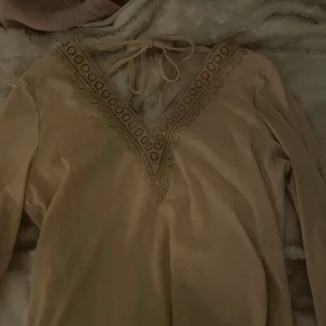 Beige topp från SHEIN med spetsdetaljer - Säljer en beige topp från SHEIN med v-ringning och spetsdetaljer. Toppen har långa ärmar och knytband i nacken. Aldrig använt den 