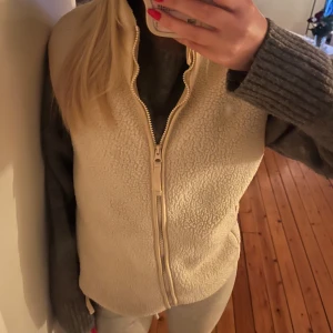 Fleeceväst  - Säljer en mysig krämvit/ beige fleeceväst med dragkedja framtill. Fickor med dragkedja. Perfket för skidresor.