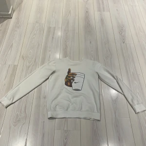 Vit sweatshirt från Nike - Säljer en vit sweatshirt från Nike med ett coolt tryck av en hand som håller en kopp. Tröjan är tillverkad i en blandning av bomull och polyester, vilket gör den både bekväm och hållbar. Perfekt för en avslappnad stil. 🏷️