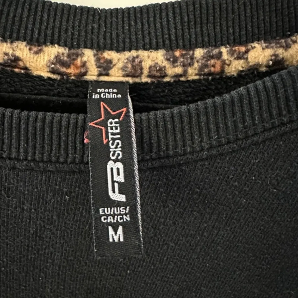 Säljer en svart sweatshirt från FB Sister med texten 'SILLY' i leopardmönster på framsidan. Tröjan har långa ärmar och en rund halsringning. Perfekt för en avslappnad stil.. Neuletakit & Villapaidat.