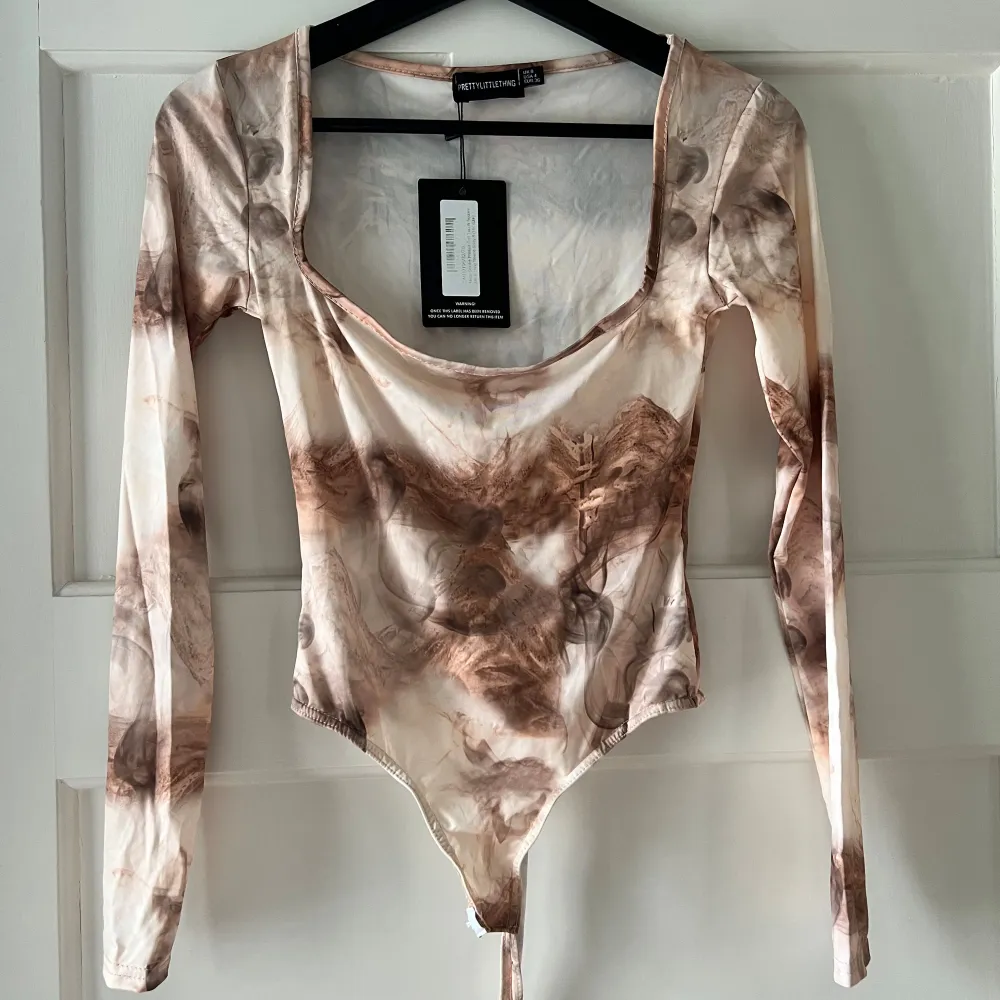 Säljer en superfin långärmad topp från PrettyLittleThing. Den har ett unikt mönster i jordnära toner som brunt och beige. Toppen är tight och har en djup rundad halsringning. Perfekt för höst och vår! Aldrig använd med prislappen kvar. . Toppar.