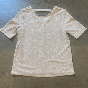 Glittrig  topp - Säljer en superfin glittrig beige/guld topp med korta ärmar. Den har en rund halsringning och ett subtilt mönster som ger en extra touch av elegans. Perfekt för festliga tillfällen!