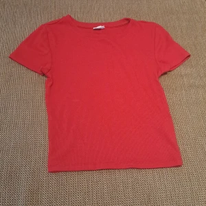 Röd ribbad t-shirt - Säljer en snygg röd ribbad t-shirt i ett mjukt och stretchigt material. Perfekt för vardagsbruk eller att styla upp för en festlig look. Den har korta ärmar och en klassisk rund halsringning.