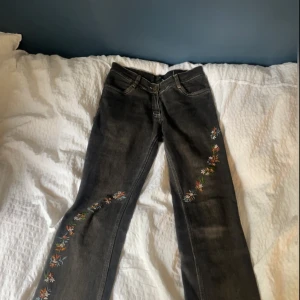 Lågmidjade jeans bootcut - Ett par urtvättade svarta jeans med lowwaist, slits och broderade blommor🌸 Kanske lite för små på mig som normalt har M (bild), men funkar bättre om man har XS/S på jeans! Hör av er för frågor eller prisförslag på dessa unika jeans 🤍