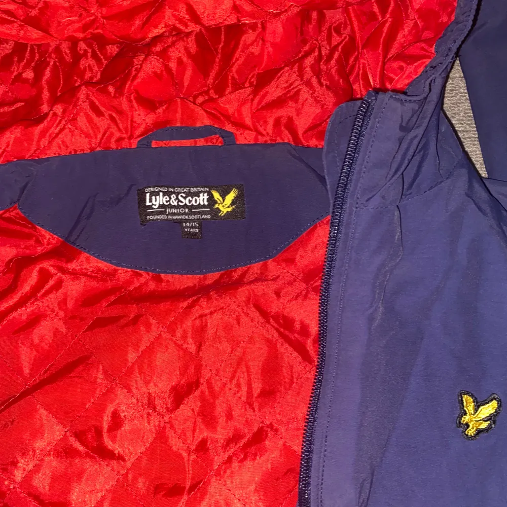 Säljer en snygg blå vindjacka från Lyle & Scott. Den har en cool röd insida och en liten gul logga på bröstet. Jackan har dragkedja och är perfekt för vår och höst. Den är i bra skick och redo för nya äventyr! Strlk xxs eller xs. Jackor.