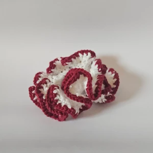 Handgjord röd och vit scrunchie - Säljer en superfin handgjord scrunchie i röd och vit färg. Den är virkad med ett vågigt mönster som ger en söt och unik look. Perfekt för att piffa upp vilken frisyr som helst! 🧶