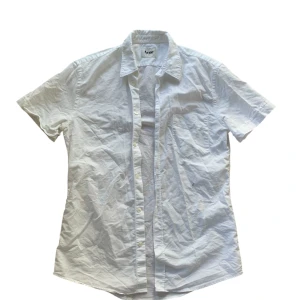 Vit kortärmad skjorta från Acne - Säljer en stilren vit kortärmad skjorta från Acne Studios . Den har en klassisk krage och knappar framtill. Skjortan är i bomull och har en diskret broderad bokstav 'A' på framsidan 