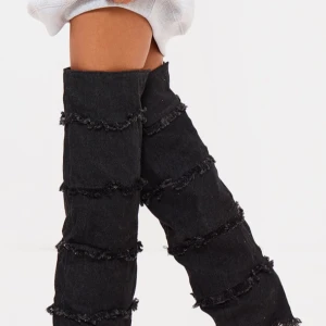 Svarta denim overknee-stövlar med spetsig tå - Dessa unika svarta denim overknee-stövlar med spetsig tå och vikbar design. Det är ett djärvt och trendigt tillskott till vilken garderob som helst. De har en distinkt design med frans detaljer i flera lager som ger en edgy och iögonfallande look. Perfekt för att lägga till en unik touch till din outfit.