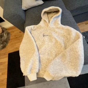 Beige fleece hoodie - Mysig beige hoodie i fleece med luva. Perfekt för kyliga dagar. Har en broderad detalj på bröstet. Passar bra för en avslappnad stil.
