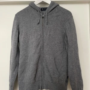 Stickad hoodie i merinoull från Riley - Säljer en stilren grå hoodie i merinoull från Riley i storlek S. Tröjan är i bra skick. Tröjan har en dragkedja framtill och en praktisk huva med snörning. Perfekt för en avslappnad look. Nypris ca 1400kr ( Jag säljer den för jag växt ur den, alldeles för liten på mig, således kan jag inte skicka en bild med den på.)